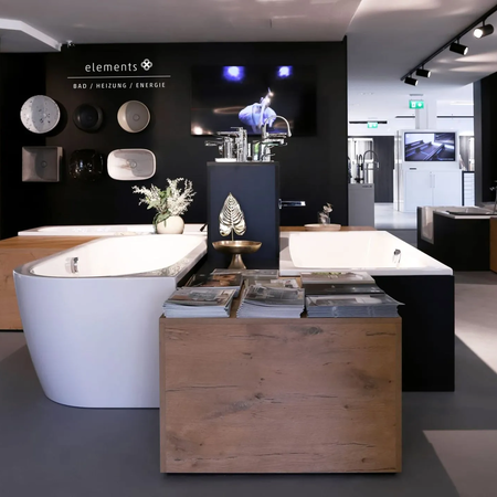 Moderne Badausstellung mit zwei freistehenden Badewannen, Holz- und schwarzen Elementen, Wand mit runden Designobjekten und Bildschirm