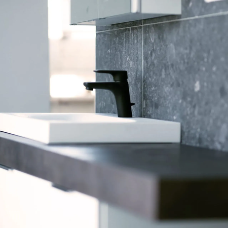 Moderner Waschtisch mit weißem rechteckigem Becken und schwarzem Wasserhahn vor grauer Wand