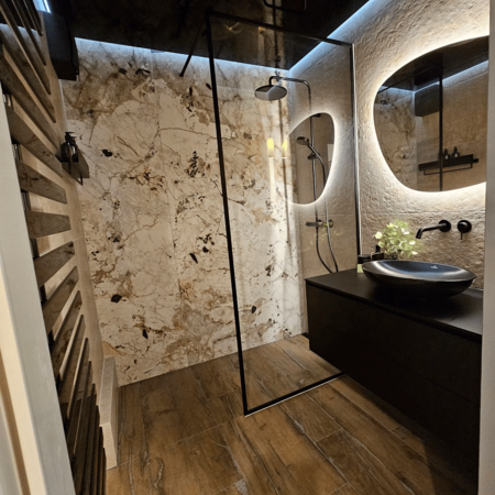 Modernes Badezimmer mit begehbarer Dusche, schwarzem Waschbecken auf schwarzer Ablage und rundem beleuchtetem Spiegel