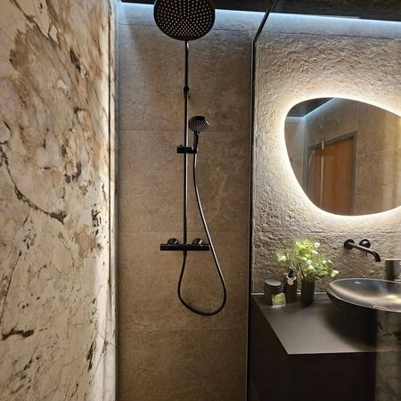 Modernes Badezimmer mit begehbarer Dusche, schwarzem Waschbecken auf schwarzer Ablage und rundem beleuchtetem Spiegel