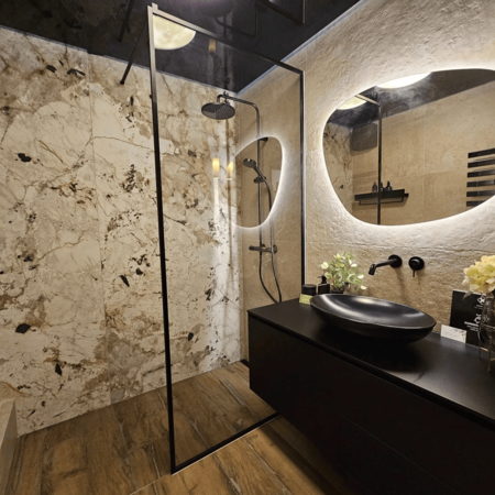 Modernes Badezimmer mit begehbarer Dusche, schwarzem Waschbecken auf schwarzer Ablage und rundem beleuchtetem Spiegel