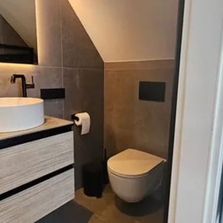 Modernes Badezimmer mit hängendem Waschbecken, beleuchtetem Spiegel und Holzschränken unter einer Dachschräge