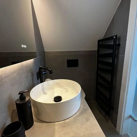 Kleines Badezimmer mit schräger Decke, weißem runden Waschbecken auf Holzunterschrank, Wand-WC und schwarzem Handtuchheizkörper