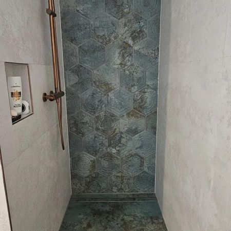 Dusche mit kupferfarbenem Duschkopf und Armatur, Wand und Boden mit blaugrauen sechseckigen Fliesen
