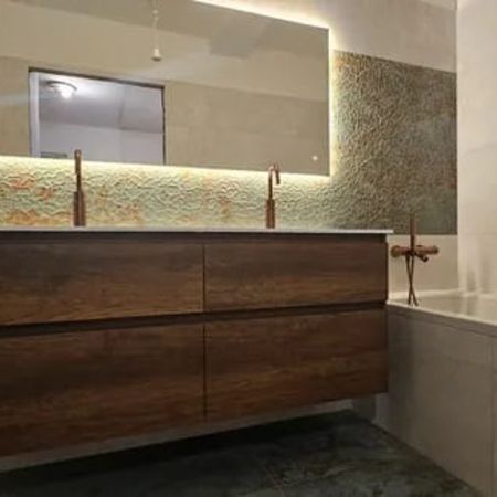 Modernes Badezimmer mit beleuchtetem Spiegel, dunklem Holzwaschtisch und Badewanne mit Wandarmatur