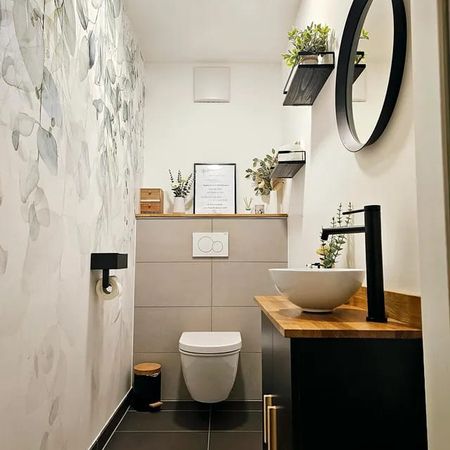 Modernes kleines Badezimmer mit hängendem WC, rundem Spiegel, Holzarbeitsplatte mit Aufsatzwaschbecken und floralen Wandmotiven