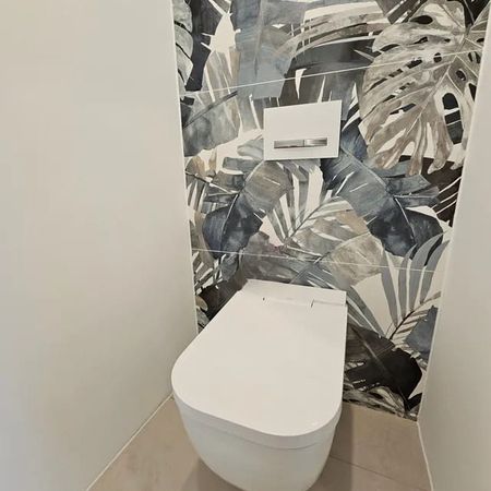Moderne weiße Wandtoilette vor Wand mit großem Blattmuster in Grautönen