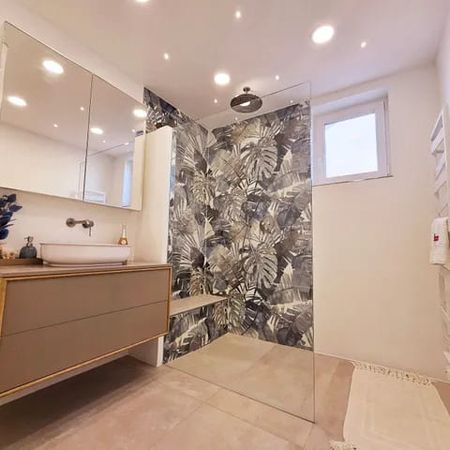 Modernes Badezimmer mit hängendem Waschtisch, großem Spiegel, begehbarer Dusche mit Glaswand und Wandfliesen mit Blattmuster