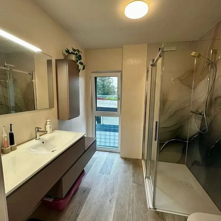Modernes Badezimmer mit Waschbecken, Spiegel, hängendem Schrank, Glasdusche und Fenster mit Blick nach draußen