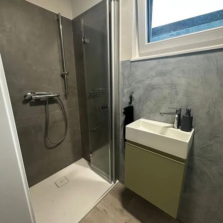 Kleine moderne Dusche mit Glasfaltwand, grauen Wänden und weißem Waschbecken mit grünem Unterschrank unter Fenster