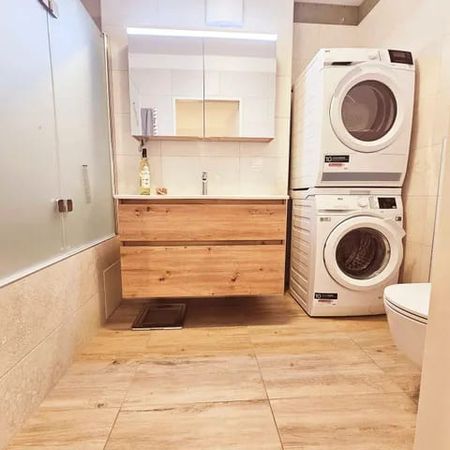 Badezimmer mit Holzwaschtisch, Spiegel mit Schrank, gestapelter Waschmaschine und Trockner, Toilette und Duschkabine