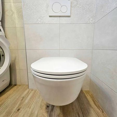 Hängendes weißes WC mit geschlossenem Deckel in modern gefliestem Badezimmer mit Holzoptikboden