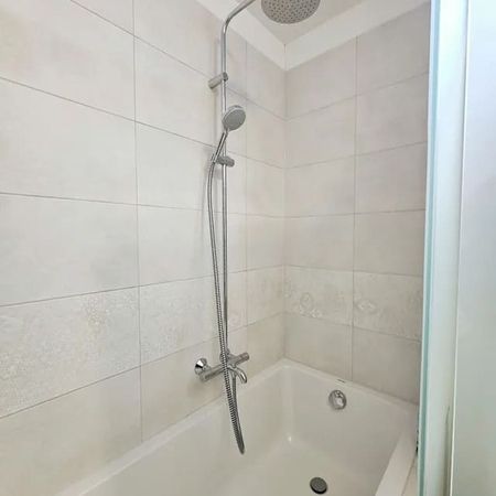 Weiß geflieste Badewanne mit Duscharmatur und Regendusche an der Wand