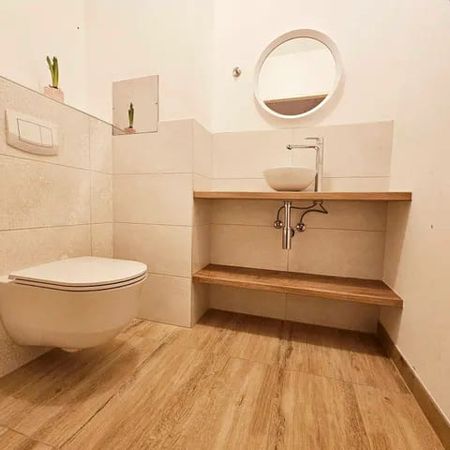 Modernes Badezimmer mit wandhängendem WC, Holzarbeitsplatte mit rundem Waschbecken und rundem Spiegel