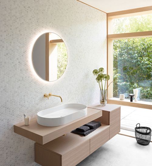 Modernes Badezimmer mit ovalem weißen Waschbecken auf Holzkonsole, rundem Spiegel und großer Fensterfront mit Blick auf Garten