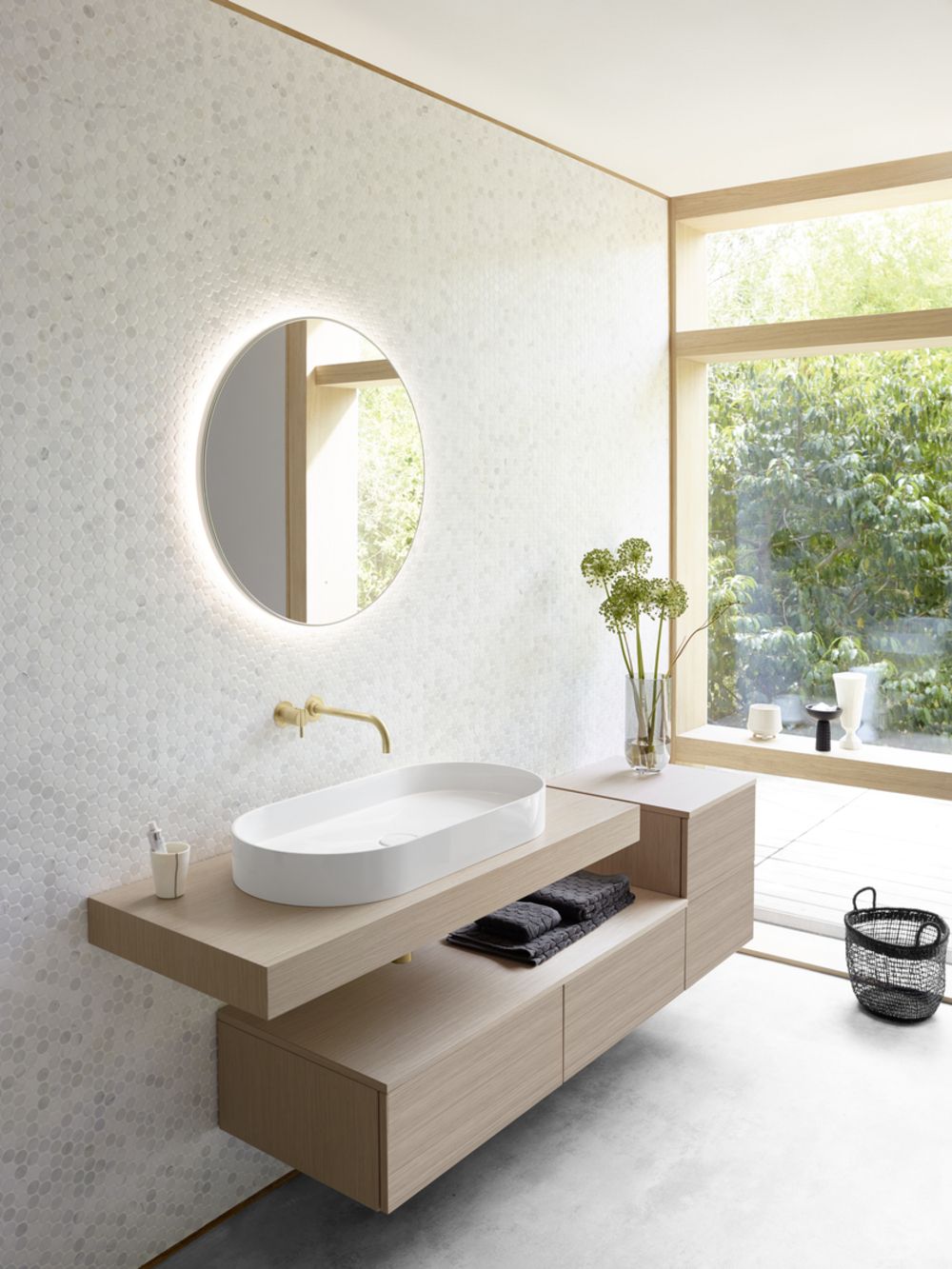 Modernes Badezimmer mit ovalem weißen Waschbecken auf Holzkonsole, rundem Spiegel und großer Fensterfront mit Blick auf Garten