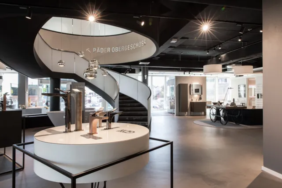 Moderner Ausstellungsraum mit spiralförmiger Treppe und verschiedenen Haushaltsgeräten auf Präsentationstischen